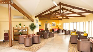 A spacious lobby with high ceilings and exposed wooden beams, furnished with wicker chairs and sofas, a bookshelf, and a large potted plant. - Lanhydrock Hotel and Golf Club (Bodmin)