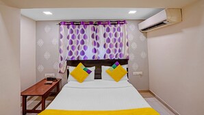 A hotel room with a bed, a bedside table, an air conditioning unit, and patterned curtains. - Itsy Hotels Aakash,100 Mts From Sardar Patel Stadium (Ahmedabad)