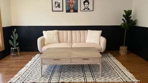 Un salón con un sofá color beige, un tapete estampado y tres cuadros en la pared.