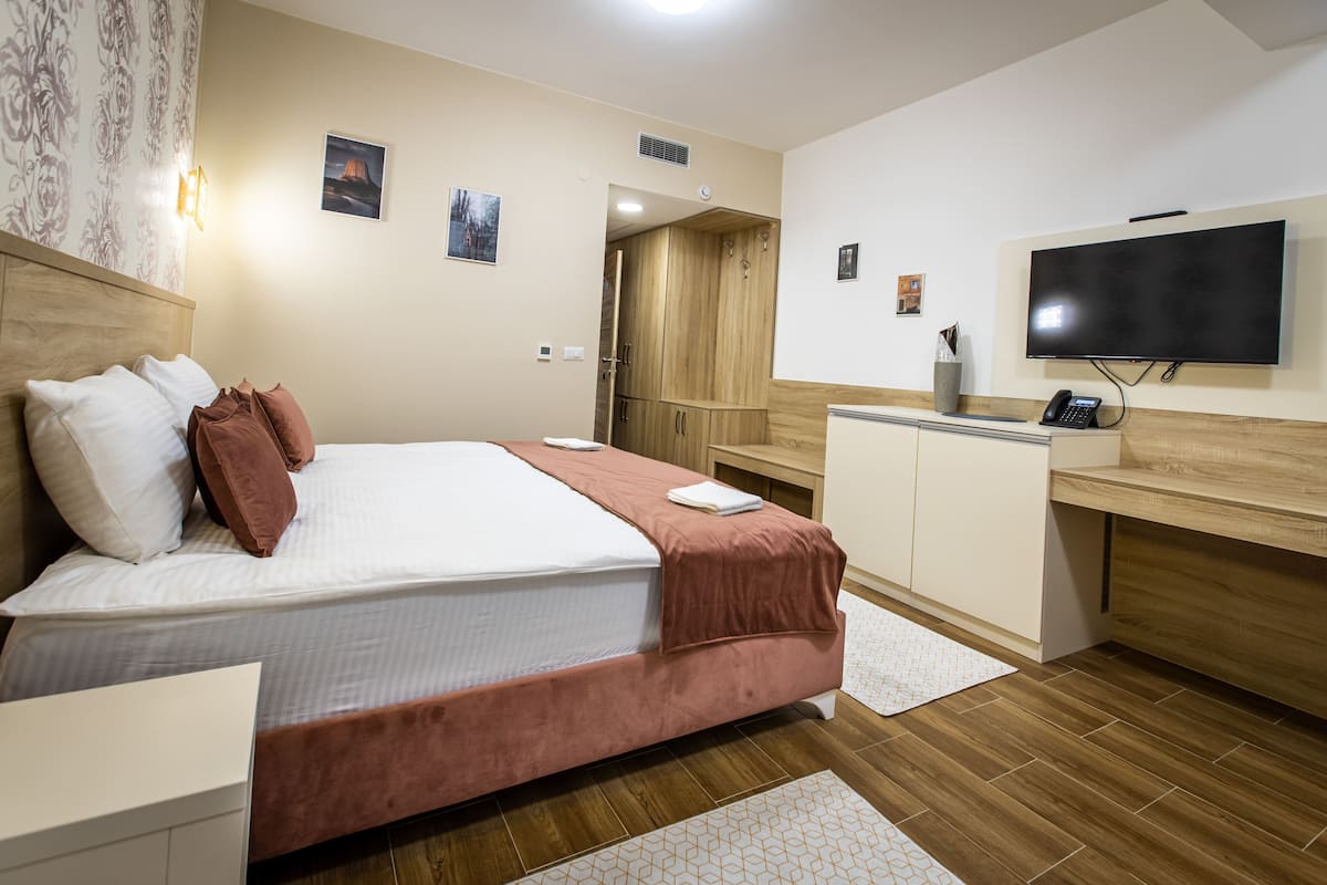 Moderni hotellihuone, jossa on suuri sänky, työpöytä, televisio ja vaatekaappi.