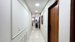 A hallway with white walls, a wooden door, and a tiled floor. - The Férias - Suítes Luxo (Cabo Frio)
