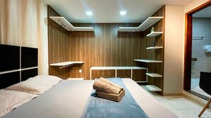 A modern bedroom with a large bed, built-in shelves, and a wooden wall panel. - The Férias - Suítes Luxo (Cabo Frio)