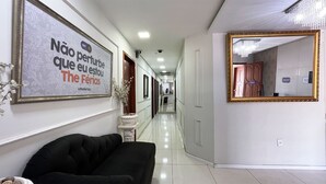 A hotel hallway with a black sofa, a large mirror, and a framed sign on the wall. - The Férias - Suítes Luxo (Cabo Frio)