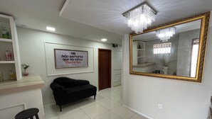 A room with a large mirror, a black sofa, a small stool, and a framed sign on the wall. - The Férias - Suítes Luxo (Cabo Frio)
