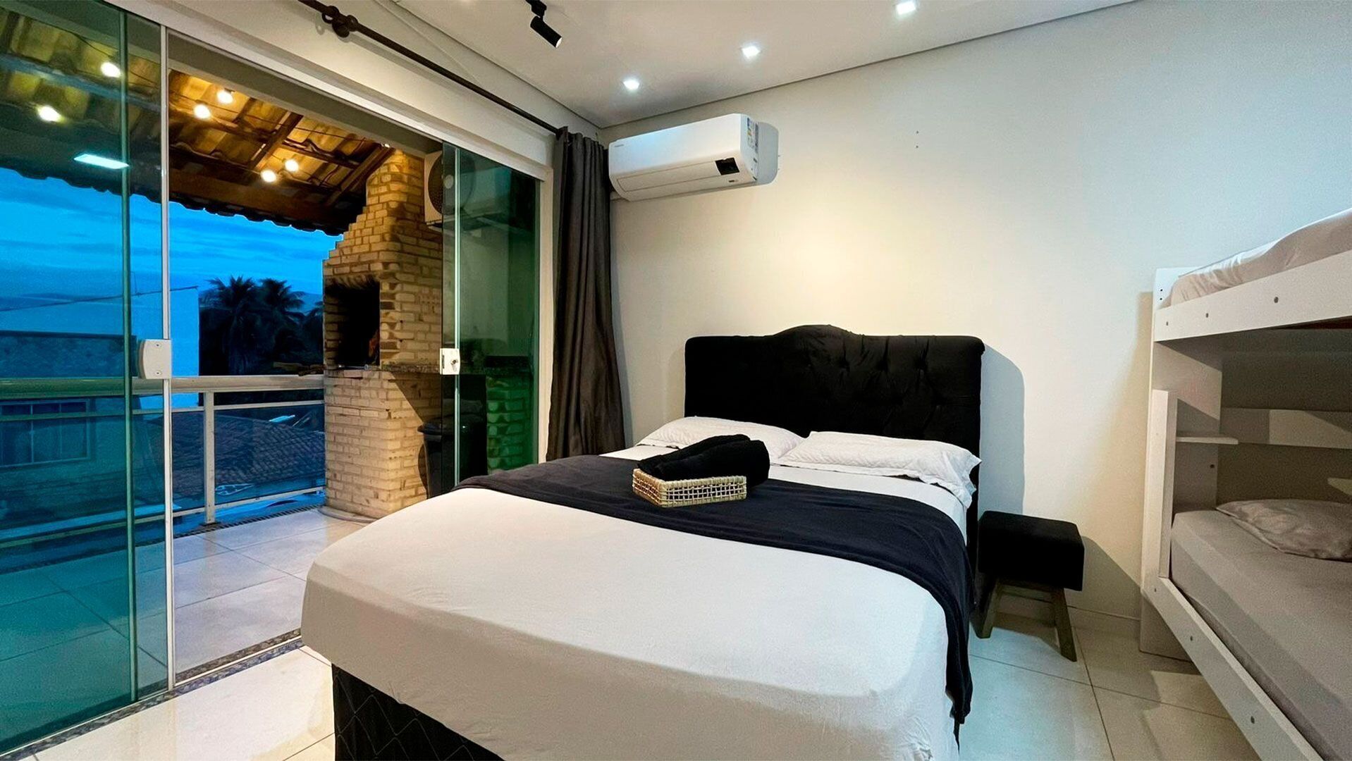A bedroom with a bed, a bunk bed, a glass door leading to a balcony, and an air conditioning unit.