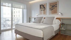 A modern bedroom with a large bed, a view of the city through a balcony, and two abstract paintings on the wall. - Nautiko by FeelFree Rentals (Donostia)