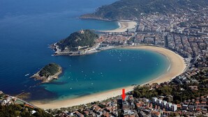 An aerial view of a coastal city with a prominent beach, a small island with a lighthouse, and dense urban development. - Nautiko by FeelFree Rentals (Donostia)