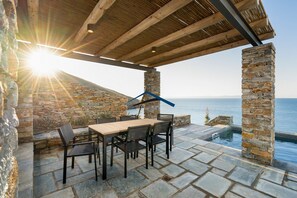 A patio with a stone table and chairs, overlooking a pool and the sea.