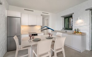 A modern kitchen with white cabinets, a stainless steel refrigerator, and a dining area with a white table and chairs.