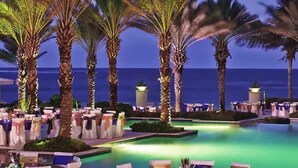 Un espace aménagé au bord de la piscine, avec des palmiers et des tables installées pour un événement, offrant une vue sur l’océan.