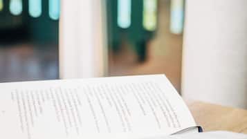 A book with text on a table next to a window with a view of trees.