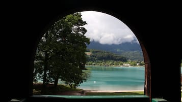 A view through an arched window of a lake with a tree in the foreground and mountains in the background.
