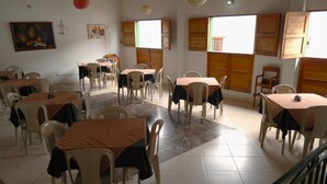 A dining area with multiple tables and chairs, large windows with wooden shutters, and artwork on the walls. - HOTEL LIDERATO (Paramo)