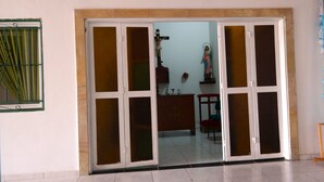 A room with a large sliding glass door leading to a balcony. Inside, there is a wooden cabinet with a cross emblem and a statue on a pedestal. - HOTEL LIDERATO (Paramo)