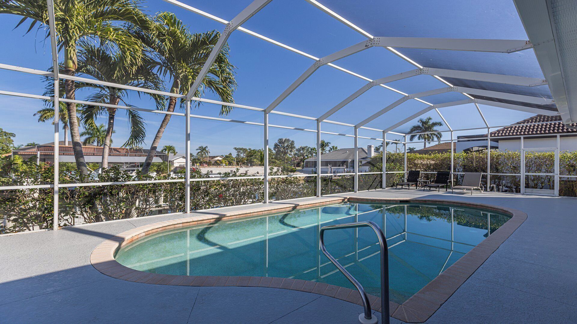 A covered swimming pool with a clear view of palm trees and houses in the background.