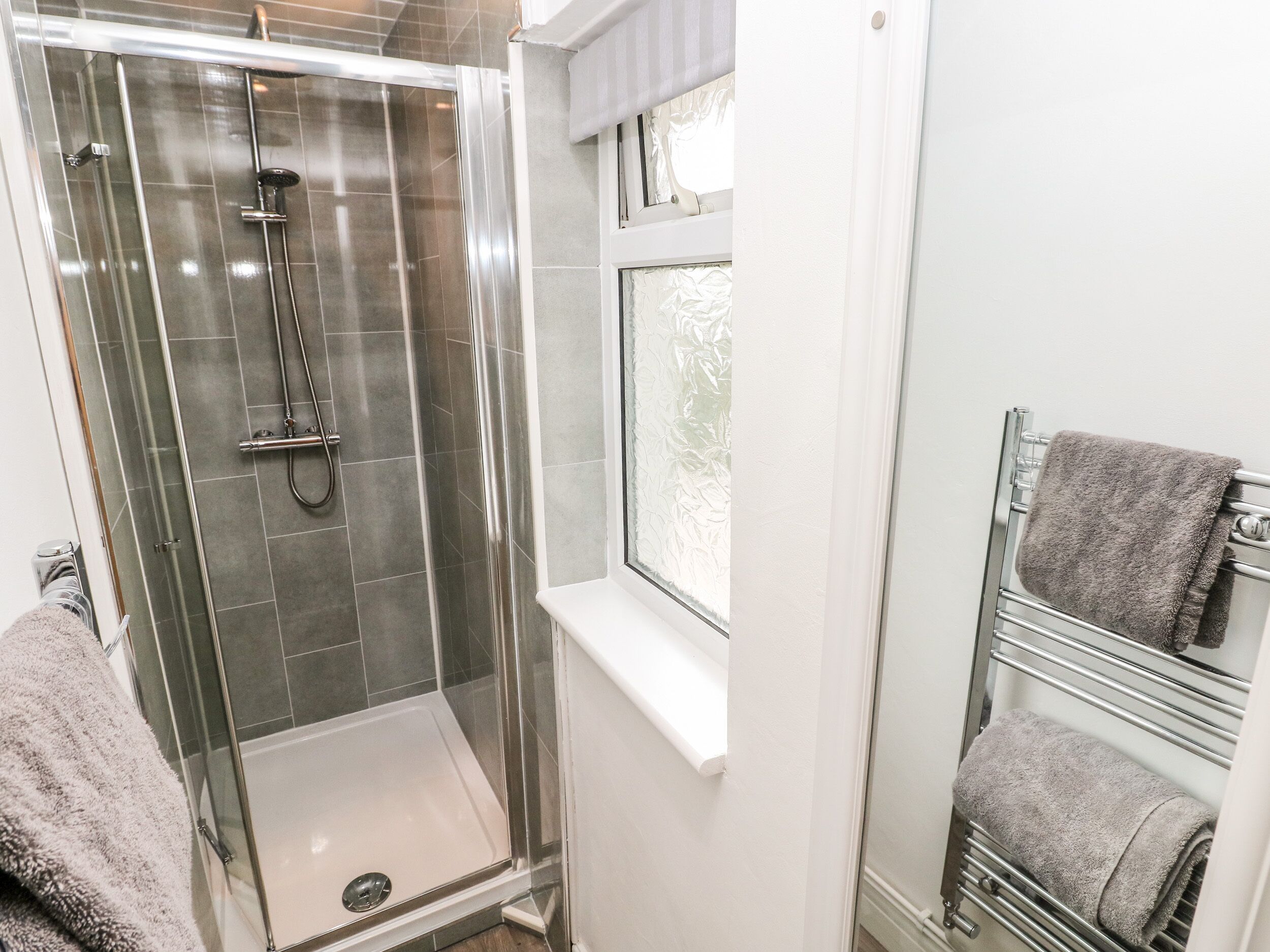 A modern bathroom with a glass-enclosed shower, a white sink, and a towel rack with towels.