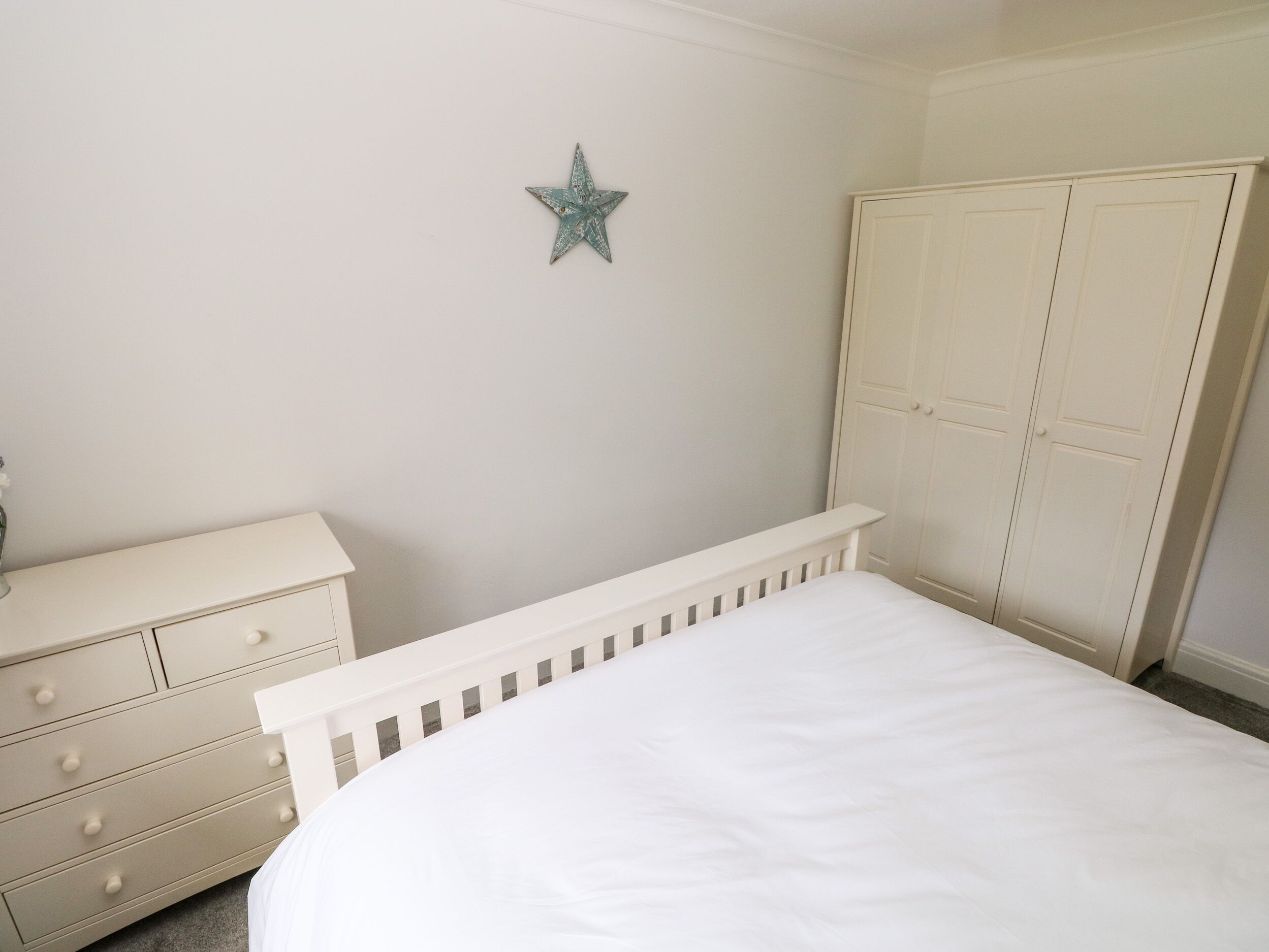 A bedroom with a white bed, a dresser with drawers, a wardrobe, and a star decoration on the wall.