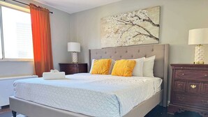 Une chambre à coucher comprenant un lit, deux tables de chevet, une commode, une fenêtre avec des rideaux et un tableau mural.