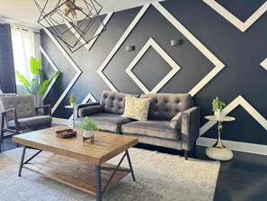 A modern living room with a sofa, armchair, coffee table, and decorative plants.