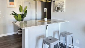 Une cuisine dotée d’un plan de travail en marbre, de deux tabourets, d’un luminaire suspendu et d’œuvres d’art murales.