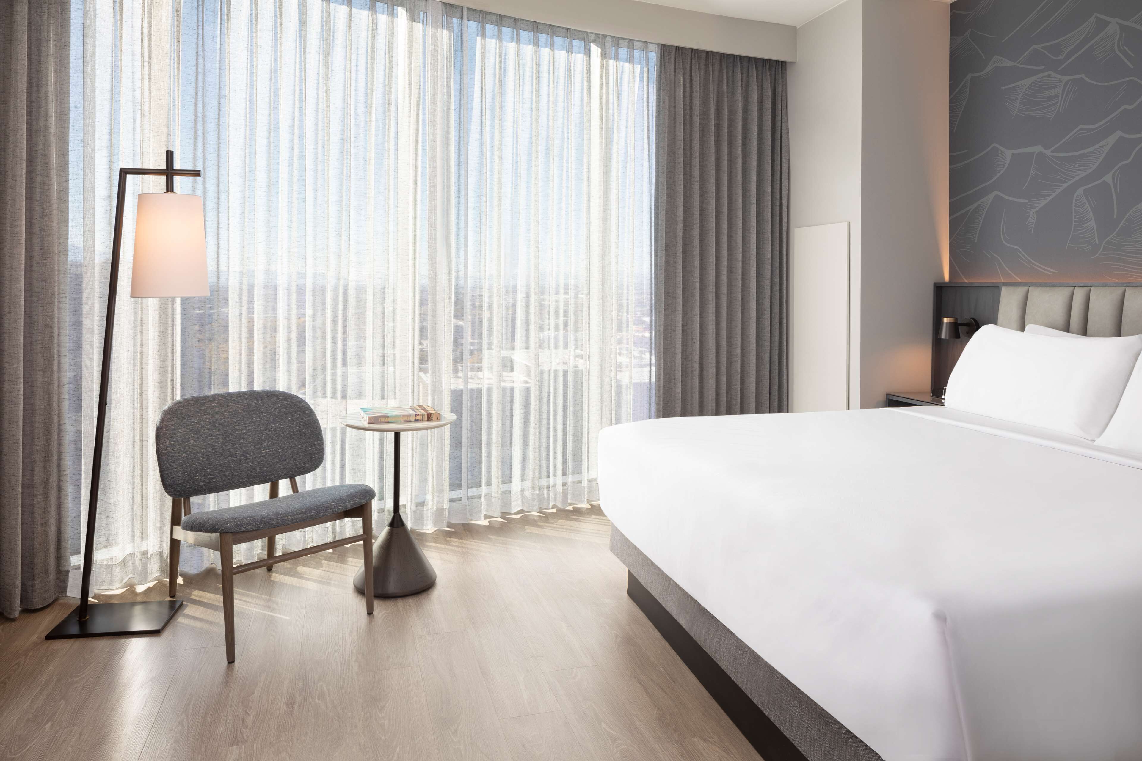 Habitación de hotel con una cama grande, una silla, una mesita y una lámpara de pie.