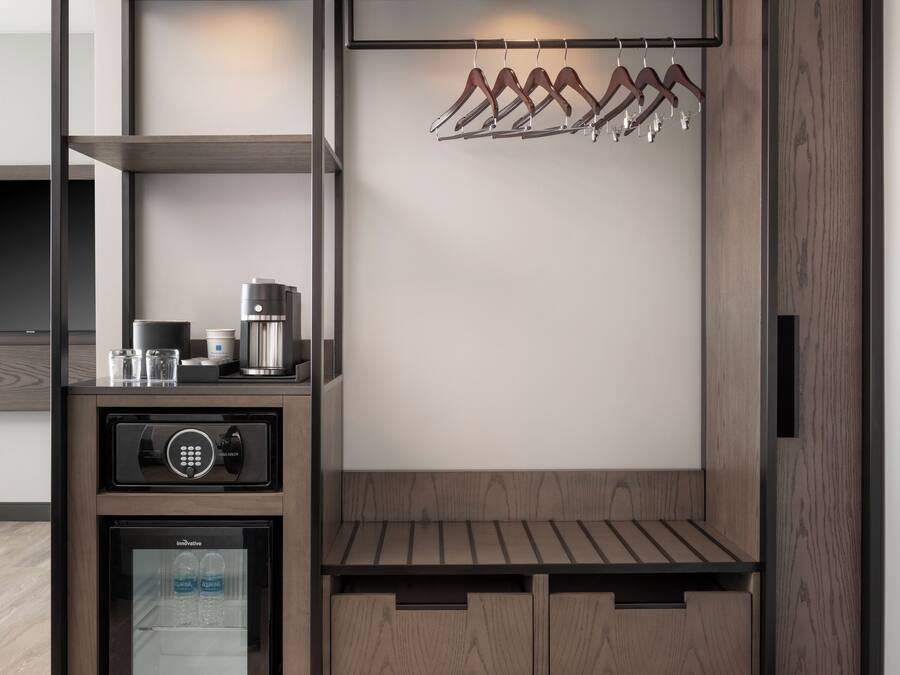 A compact, modern room with a built-in wardrobe, a coffee machine, and a mini-fridge.