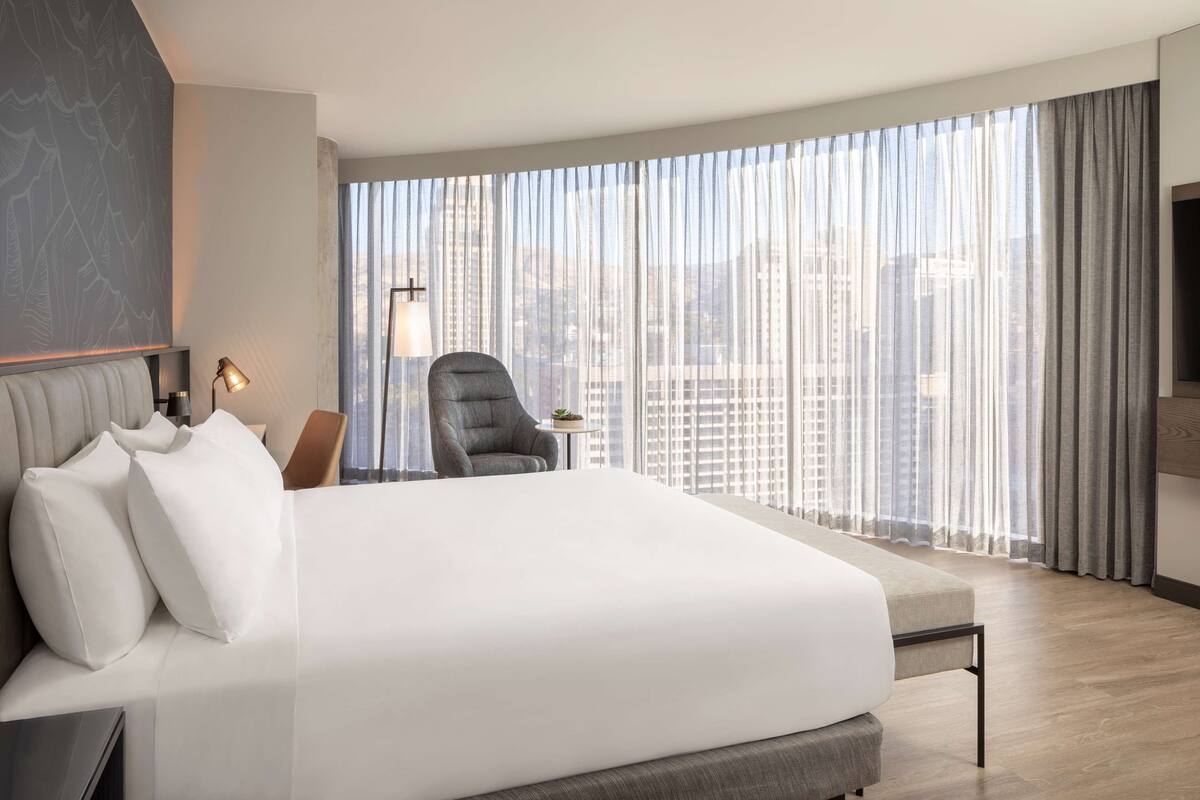 Une chambre d’hôtel moderne avec un grand lit, une chaise, une petite table et un téléviseur.