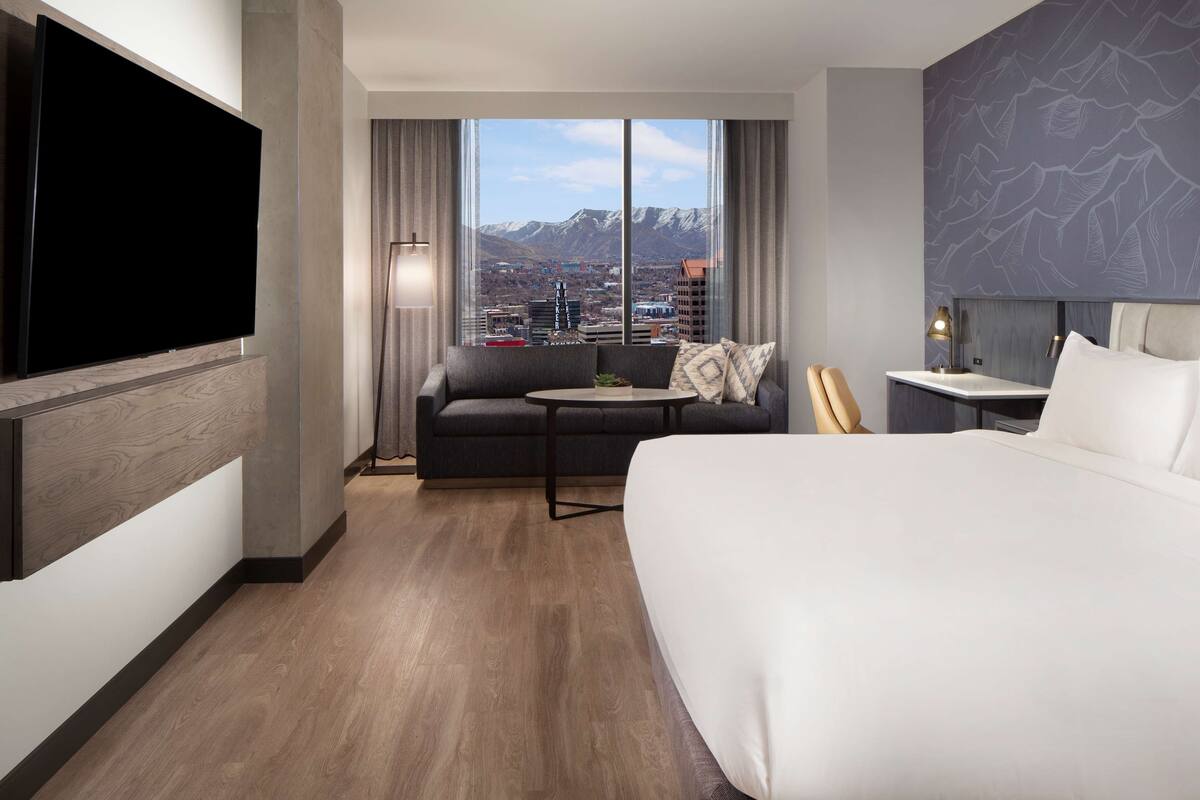 Une chambre d’hôtel avec un grand lit, un canapé, une petite table, une télévision et une vue sur la ville.