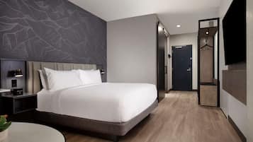 A modern hotel room with a large bed, a flat-screen TV, a bedside table with a lamp, and a wall-mounted TV.