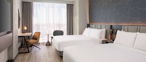 A hotel room with two beds, a desk, a chair, a lamp, and a large window with curtains.