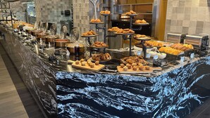 Un mostrador de buffet con diversos alimentos, incluyendo pasteles y productos horneados, dispuestos en soportes escalonados y bandejas.
