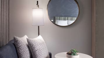 Een moderne woonkamer met een grijze bank, gestreepte kussens, een ronde spiegel, een vloerlamp en een klein tafeltje met een vetplant.