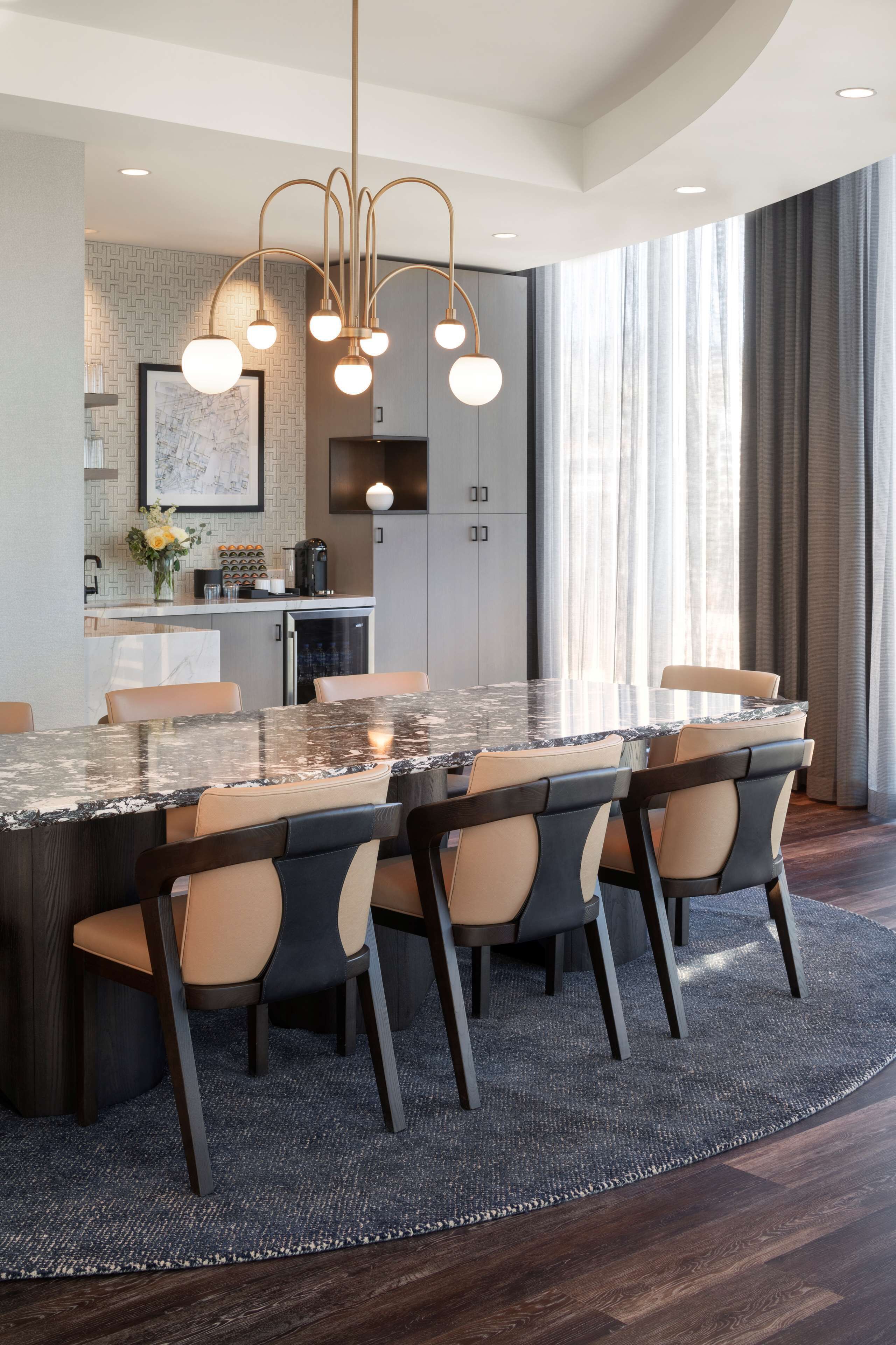 A modern kitchen with a marble island, pendant lighting, and a view of the living area.