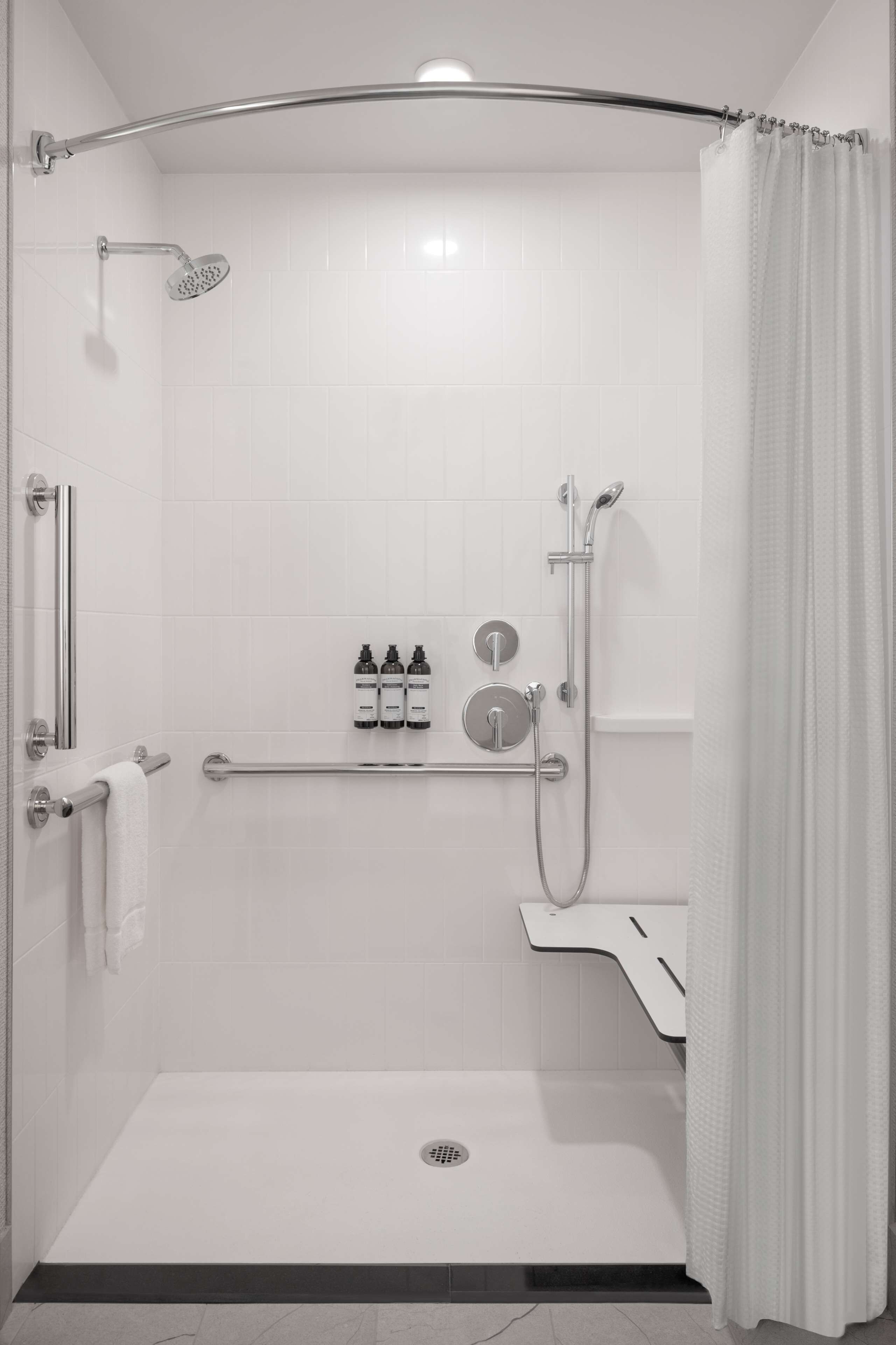 A modern shower area with a grab bar, a handheld showerhead, a wall-mounted faucet, and a toilet with a bidet attachment.