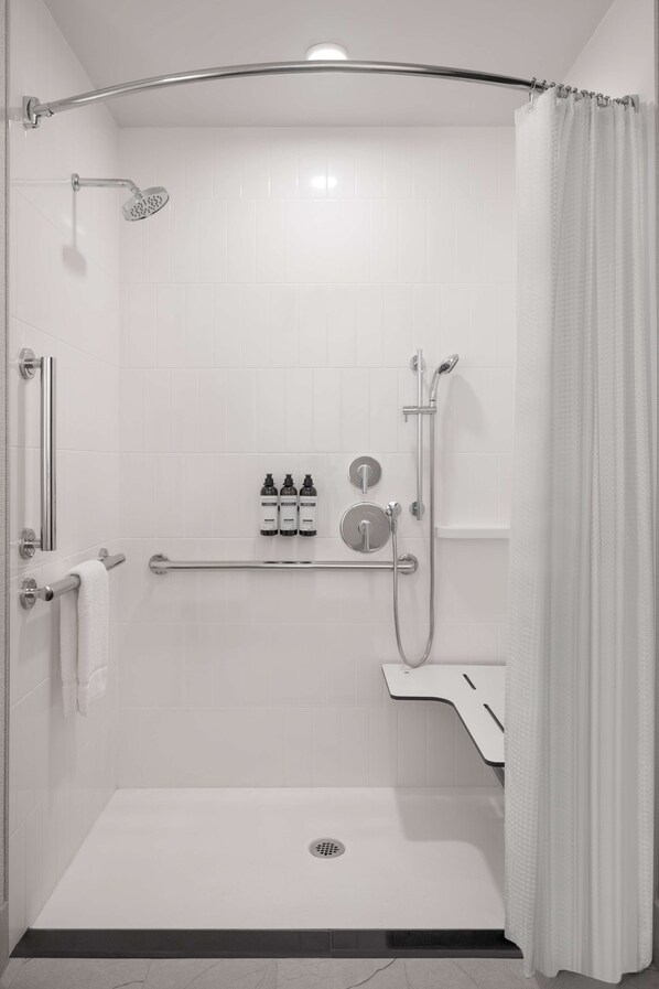 A modern shower area with a grab bar, a handheld showerhead, a wall-mounted faucet, and a toilet with a bidet attachment.