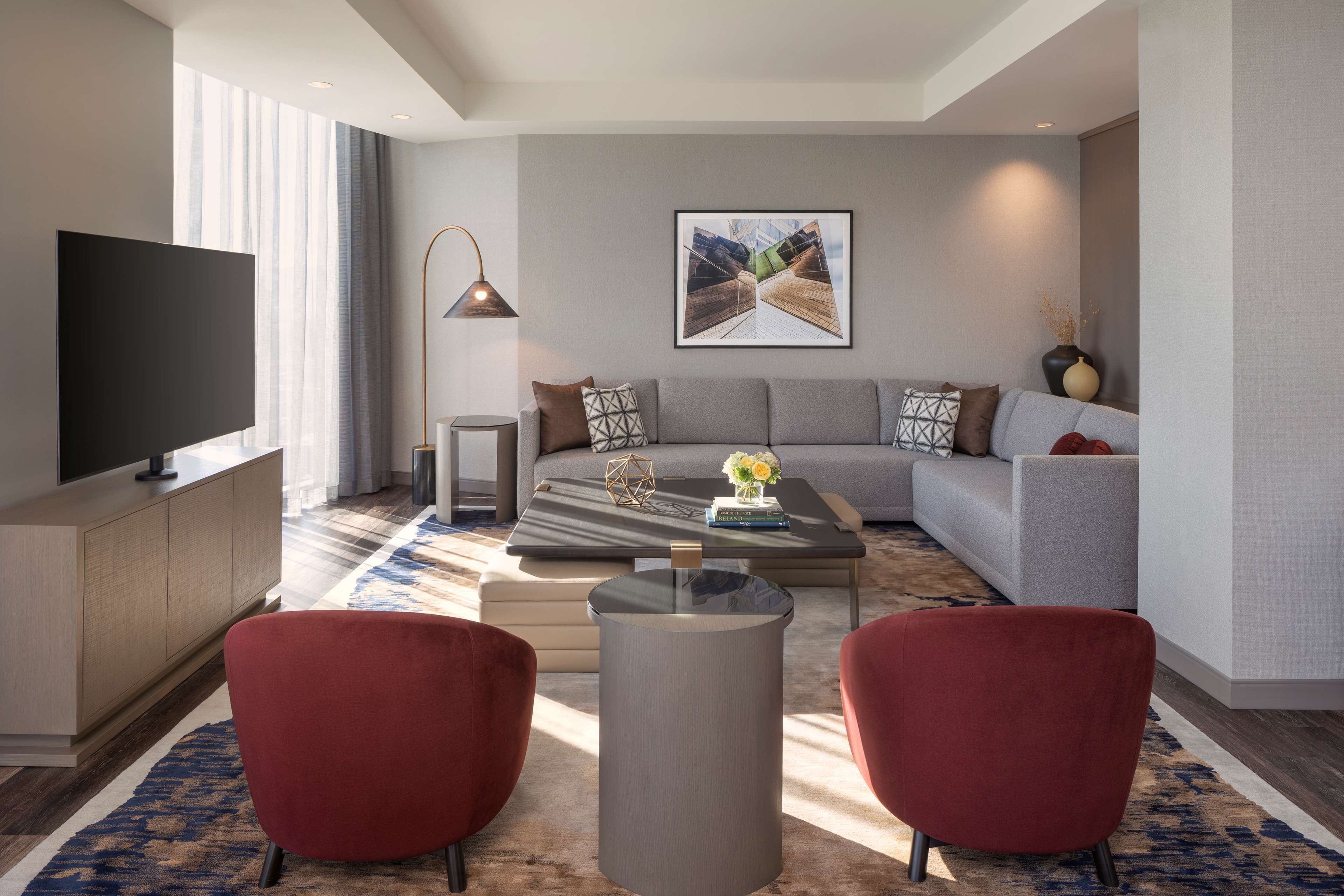 A modern living room with a sectional sofa, a flat-screen TV, a coffee table, and two red armchairs.
