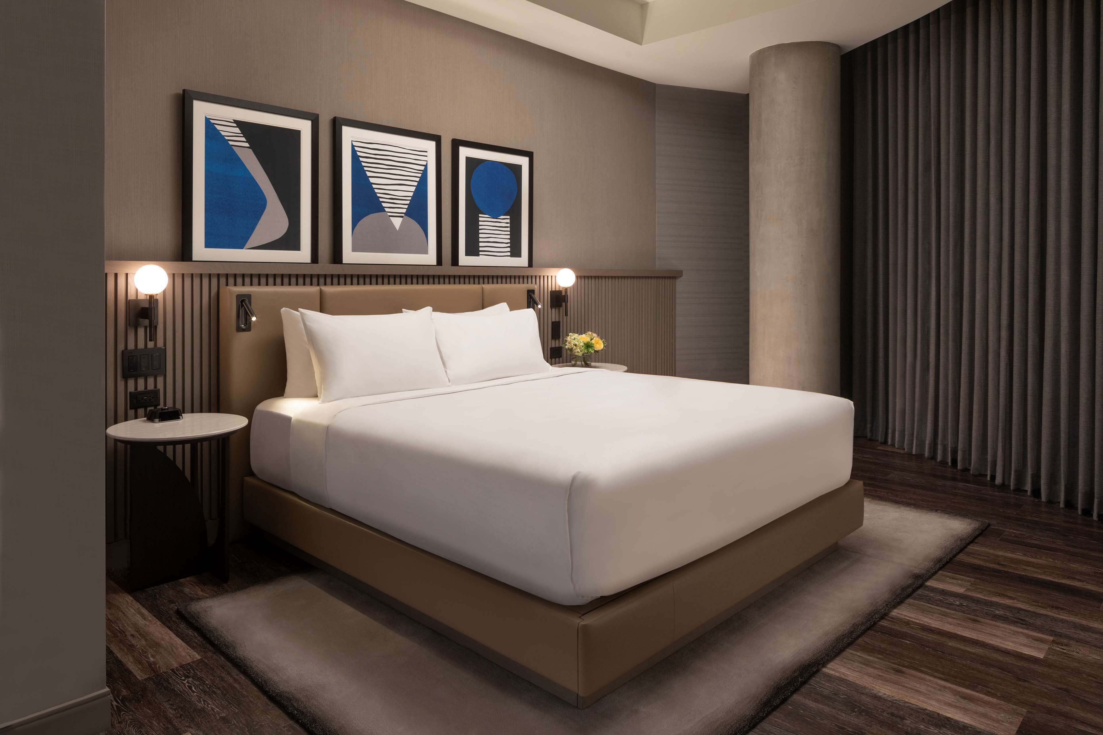 Una habitación de hotel moderna con una cama grande, una mesita de noche redonda y una lámpara de pared.