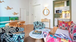 Una sala de estar moderna con un sofá, sillas, una mesa de centro y una zona de cocina con microondas y armarios.
