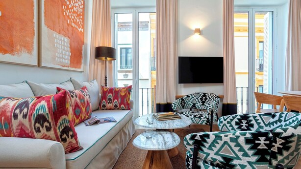 Una sala de estar con sofá, sillón y reposapiés, una mesa redonda de centro y un televisor de pantalla plana.