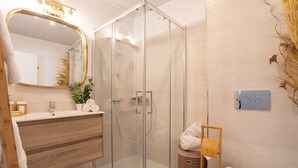 A modern bathroom with a glass-enclosed shower, a wooden vanity, a large mirror, and a wall-mounted light fixture. - Genteel Home Mercado Central Terrace (Cadiz)