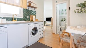 A modern kitchen with a built-in washing machine, a wooden countertop, and a dining area with clear chairs. - Genteel Home Mercado Central Terrace (Cadiz)
