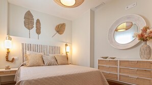 A bedroom with a large bed, a bedside table with a lamp, a wall-mounted mirror, and decorative leaves. - Genteel Home Mercado Central Terrace (Cadiz)