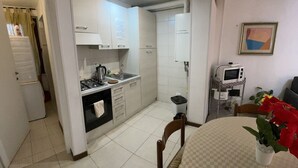 Una cocina funcional con armarios blancos, una estufa y un lavabo. Hay una mesa de comedor con un jarrón de flores.