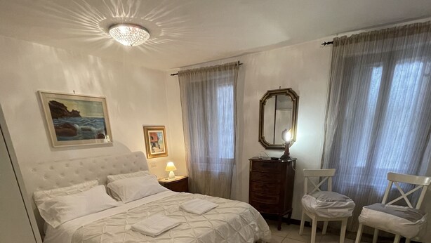 Un dormitorio con cama, mesita de noche, cómoda, silla y un cuadro en la pared.