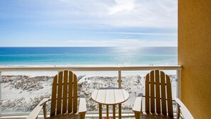 Un balcón con dos sillas Adirondack y una mesita, con vista a una playa y una vista despejada del océano.
