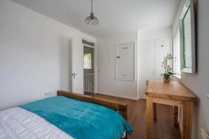 Quarto com cama, um banco de madeira, uma mesa com planta e porta para outro cômodo.