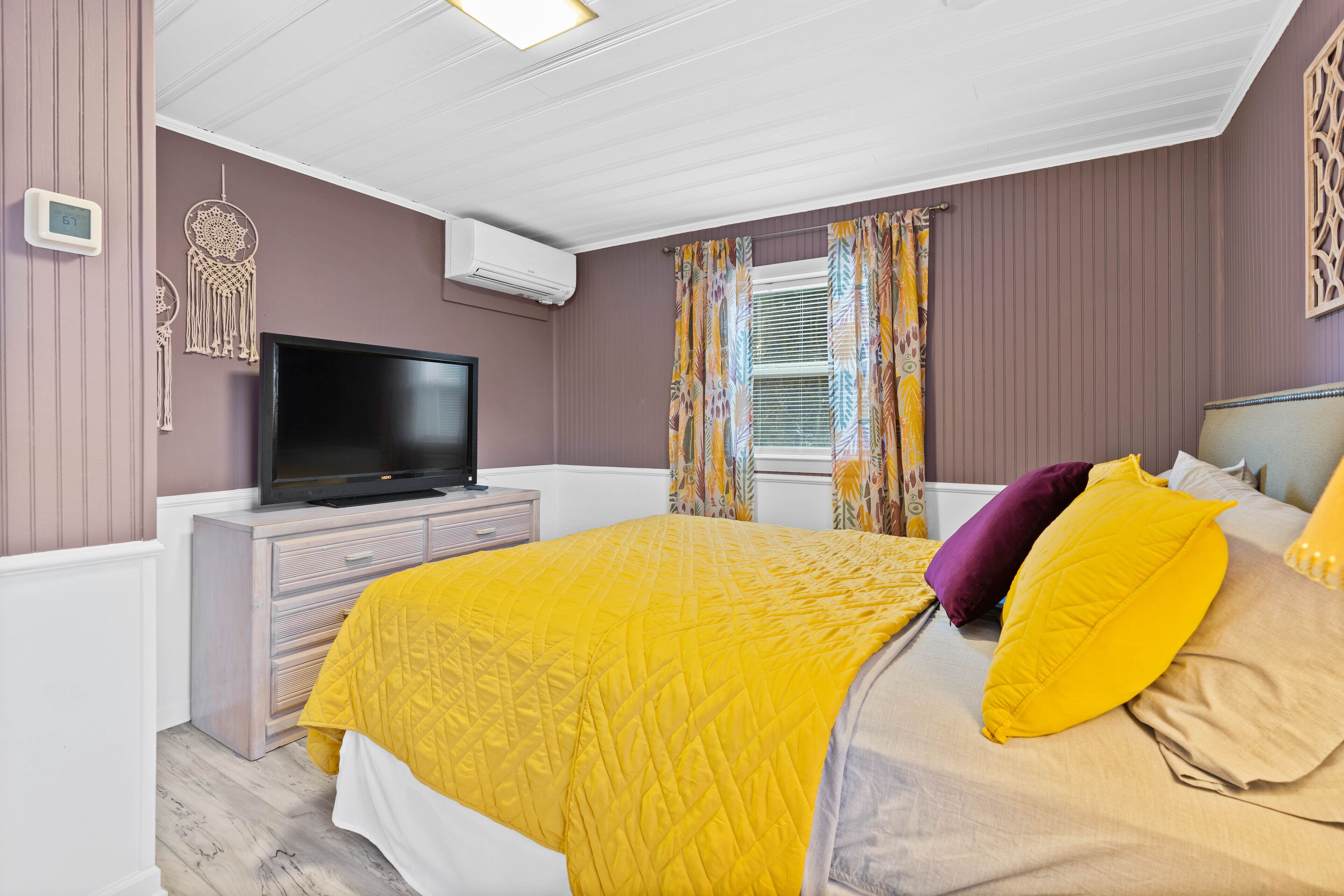A bedroom with a bed, a television, a dresser, and a window with curtains.
