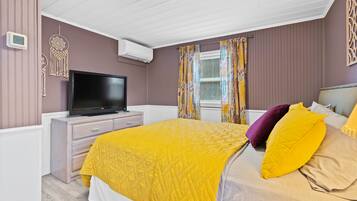 A bedroom with a bed, a television, a dresser, and a window with curtains.