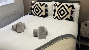 A neatly made bed with patterned pillows, a framed artwork above it, and a window to the left.
