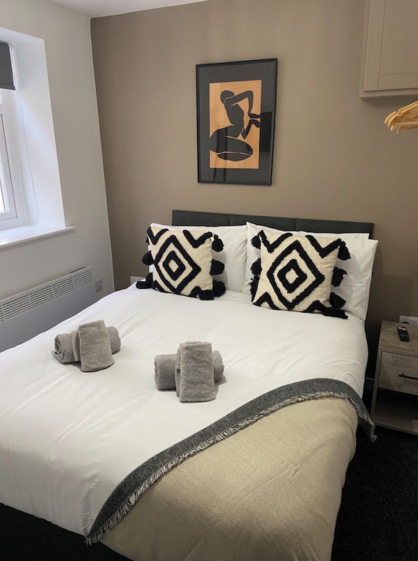 A neatly made bed with patterned pillows, a framed artwork above it, and a window to the left.
